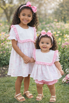 Two young girls in matching pink and white dresses standing in a garden.