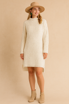 Woman wearing a cream-colored dress with long sleeves and a hat on a beige background