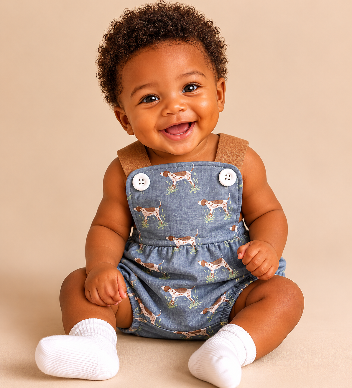Baby wearing a denim blue bubble with dog pattern on a beige background