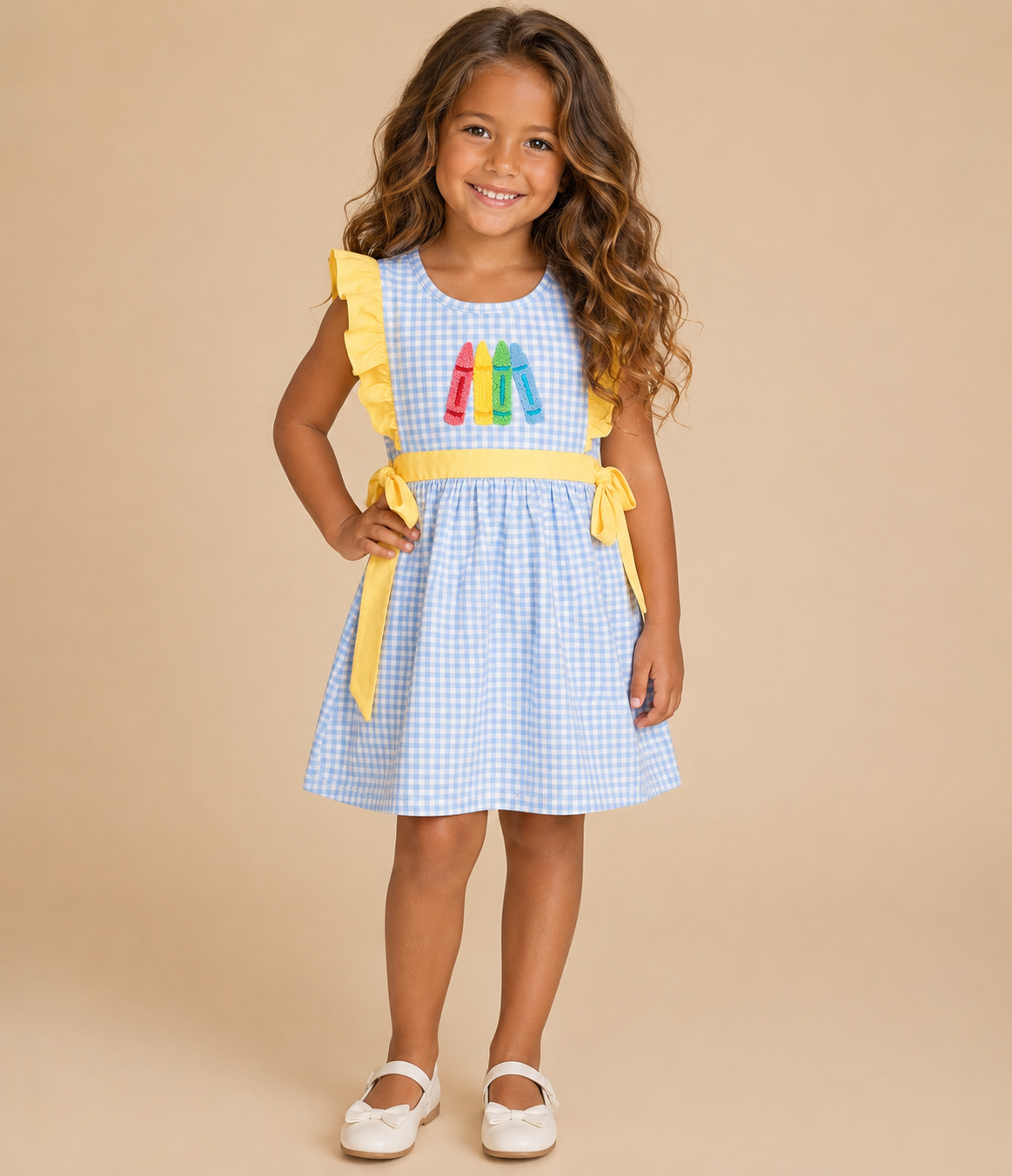 Young girl wearing a light blue gingham dress with crayons embroidered on the front.