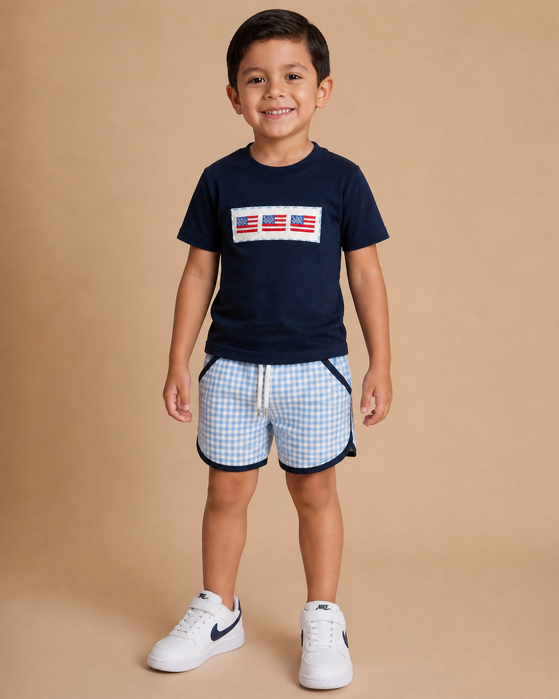 Boy wearing a navy shirt with three flags on the front with gingham shorts.
