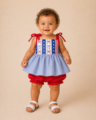 Baby wearing a patriotic outfit with a red, white, and blue design on a beige background