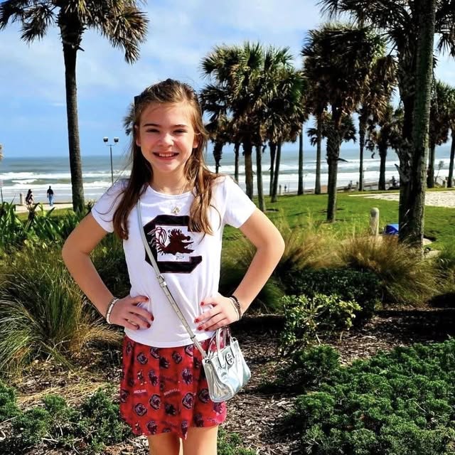 Young girl standing outdoors with palm trees and ocean in the background