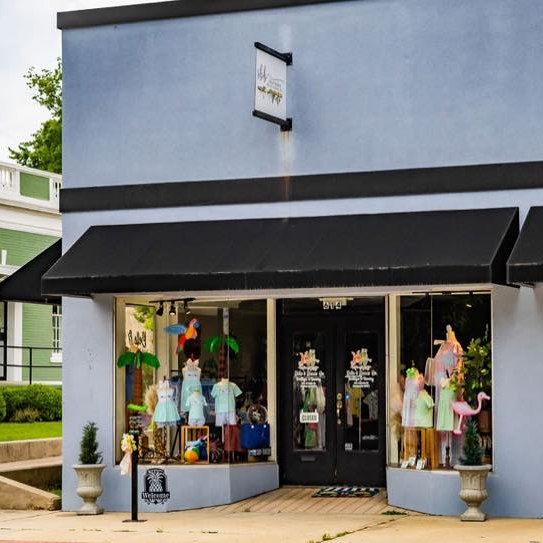 Storefront with mannequins wearing colorful outfits and a black awning.