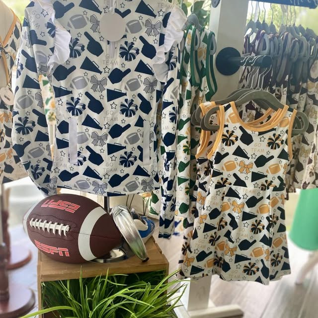 Children's clothing with sports-themed design on hangers in a store setting.