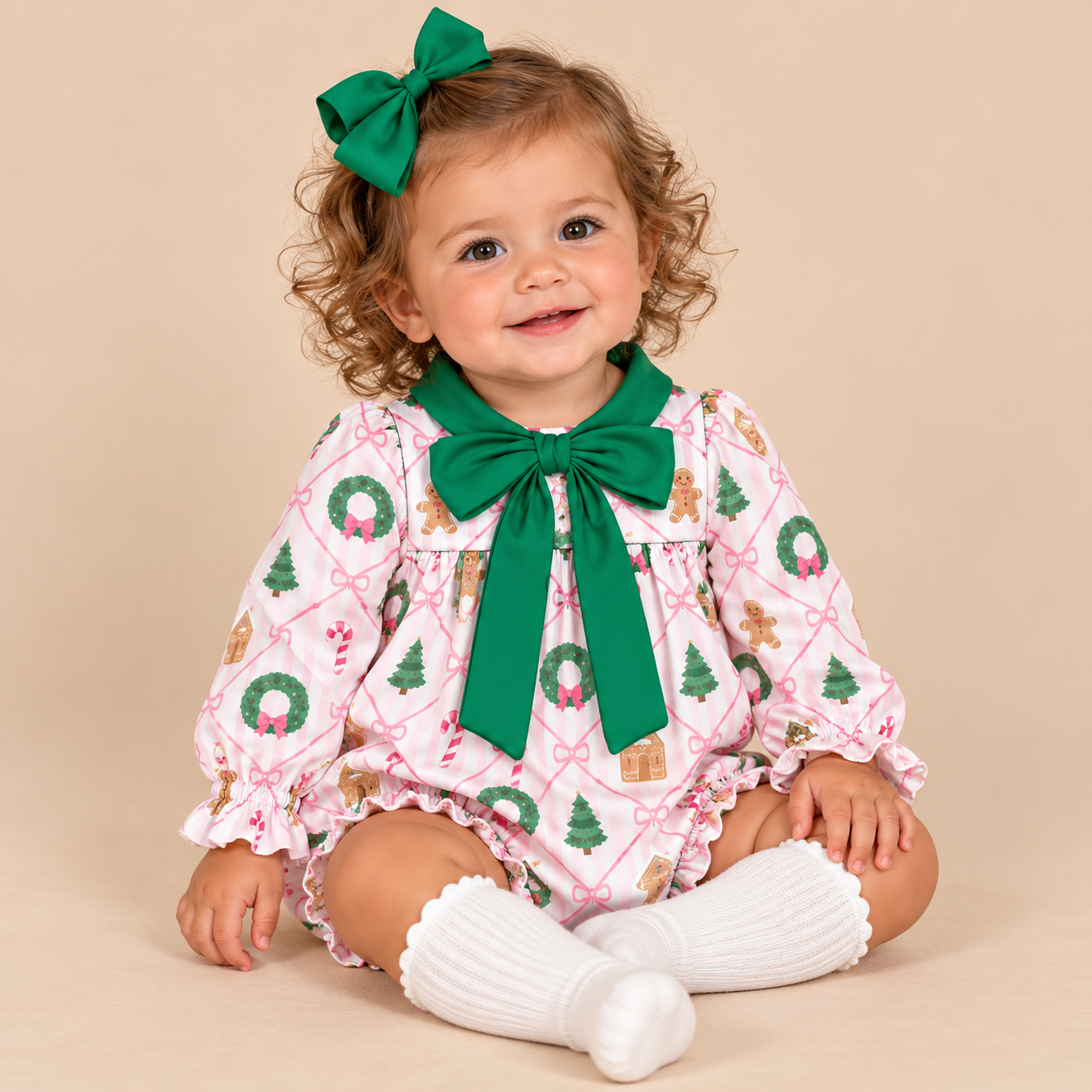Baby girl model sitting wearing a wreath and gingerbread man print bubble with a green bow around the neck.
