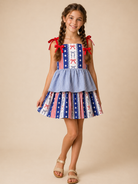 Young girl wearing a patriotic dress with red, white, and blue patterns on a beige background