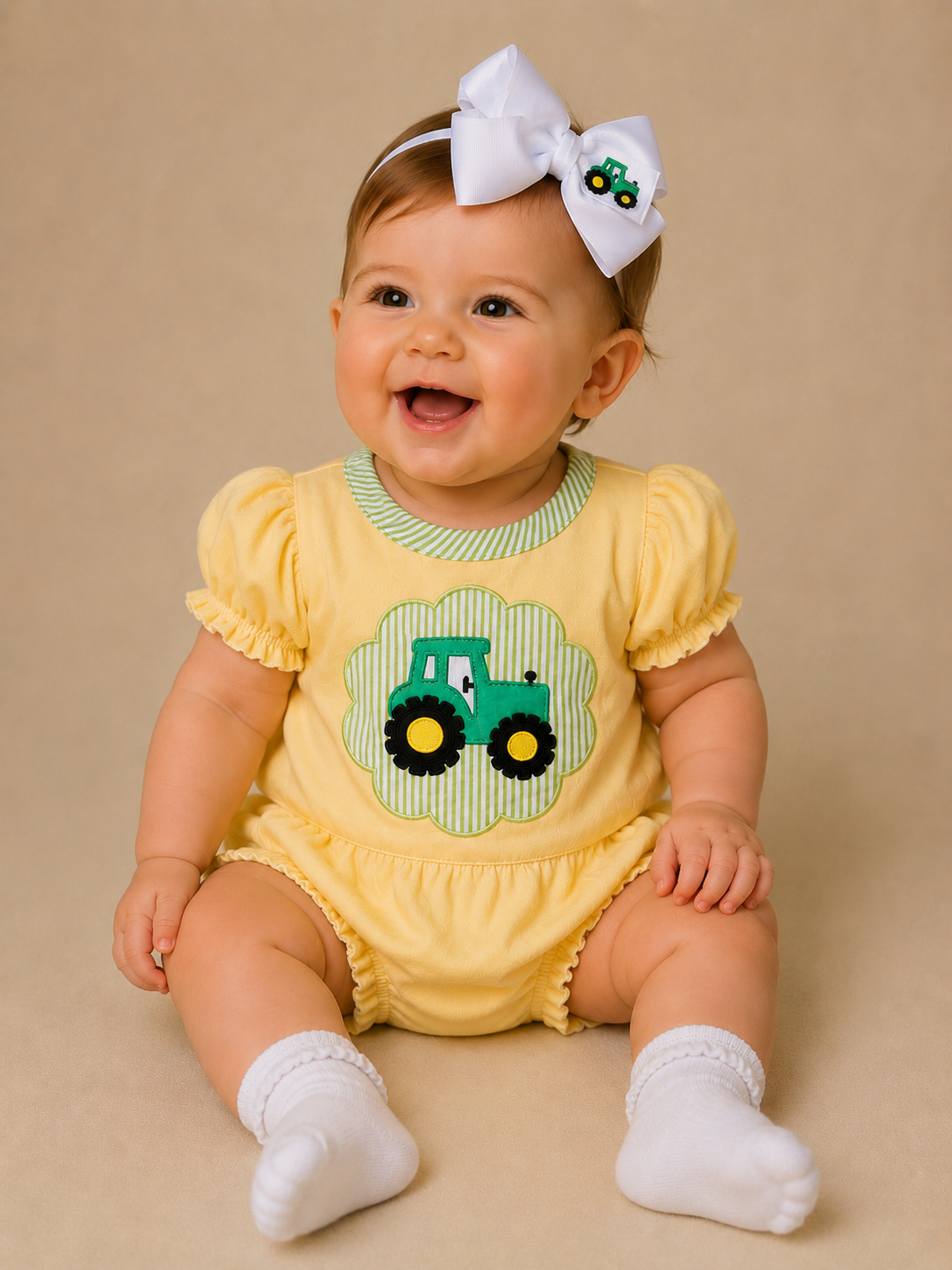 Baby wearing a yellow bubble with a green tractor design on a beige background