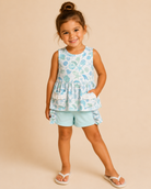 Young girl wearing a floral top and light blue shorts on a beige background