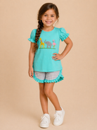 Young girl wearing a turquoise top with animal prints and checkered shorts on a beige background