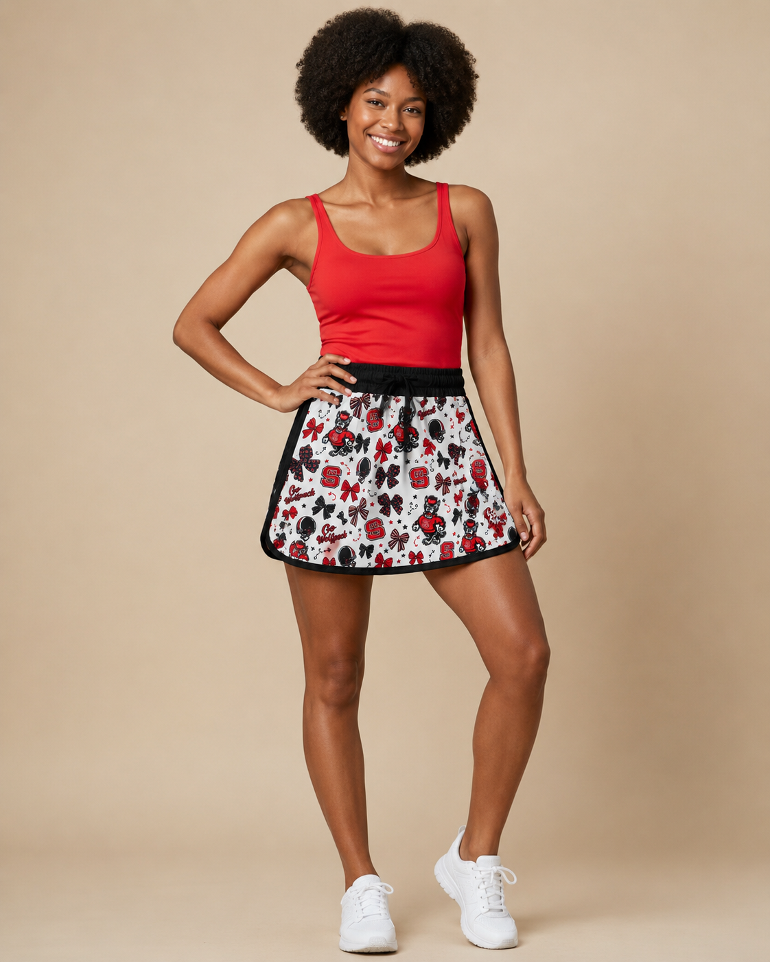Lady wearing a red tank top and a NC State printed skort with white tennis shoes.