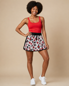 Lady wearing a red tank top and a NC State printed skort with white tennis shoes.