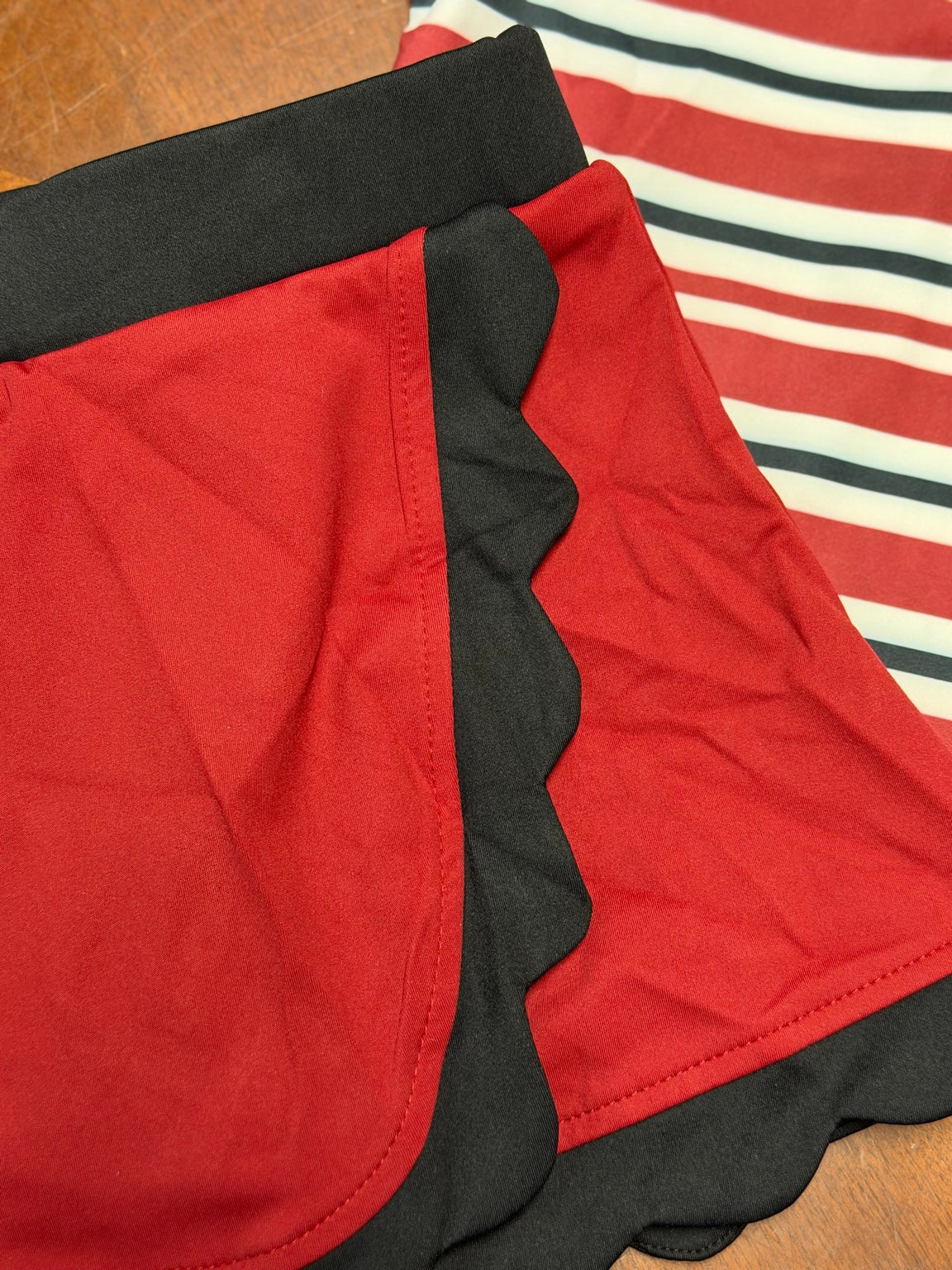 Detail shot of garnet and black stripe mascot skort set fabric and scallop trim
