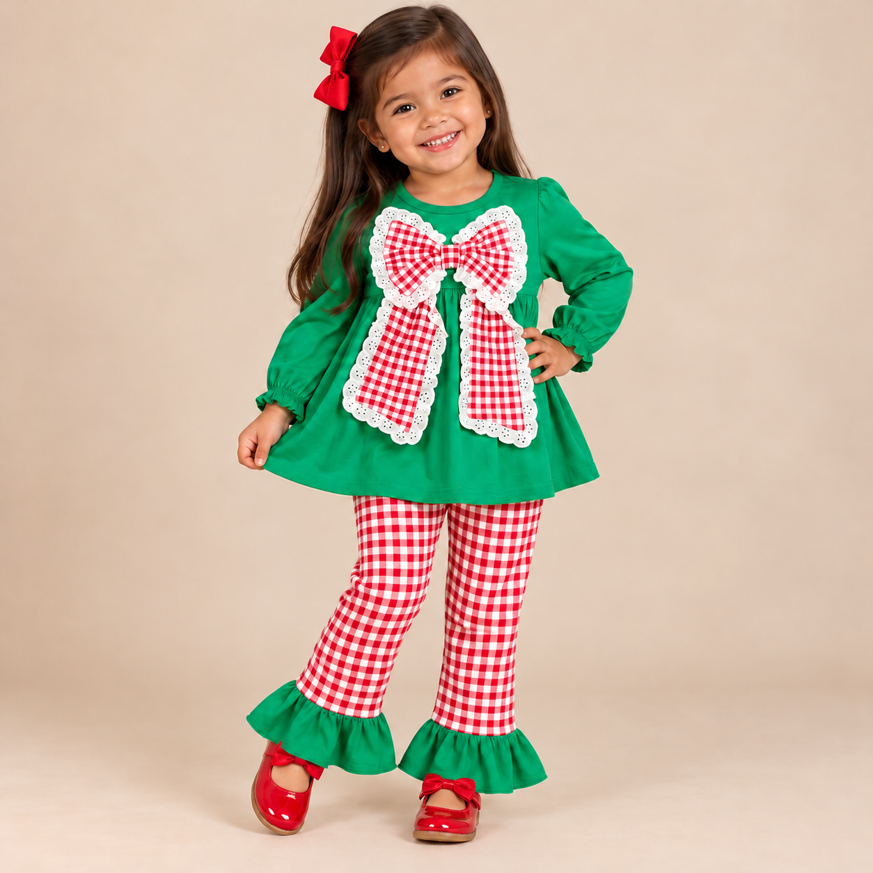 Toddler girl wearing a long sleeve green top with a big red & white gingham bow with matching gingham pants.