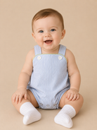 Baby wearing a blue striped romper sitting on a beige background