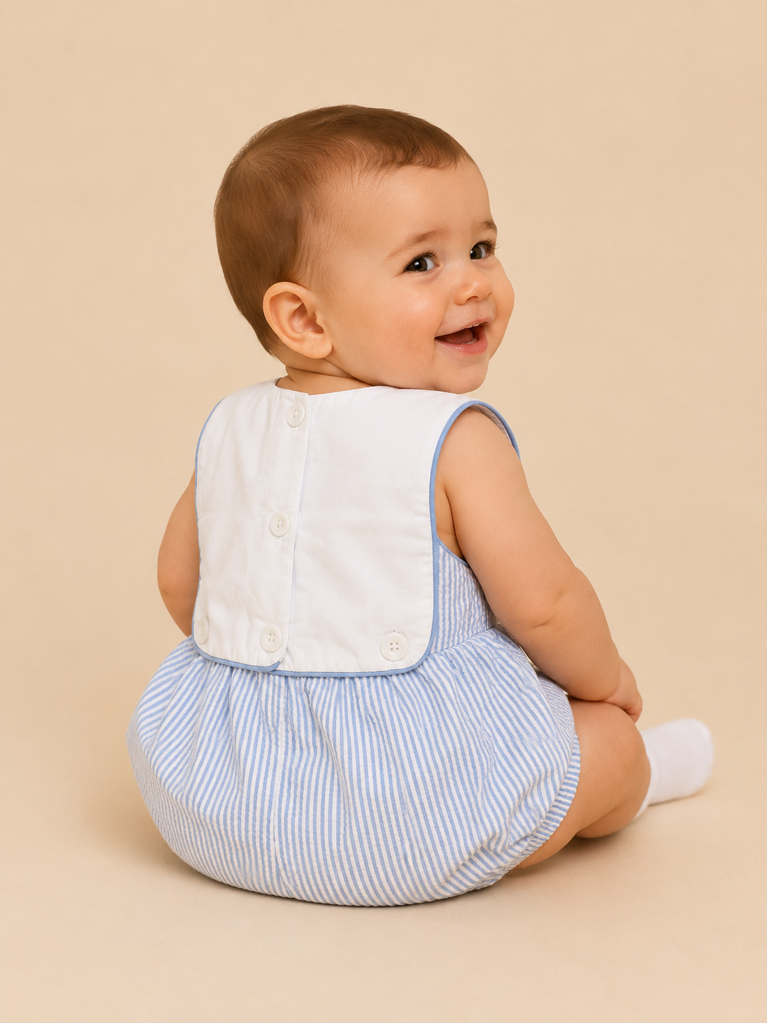 A baby wearing a light blue and white striped romper with a white bib, sitting against a solid beige background.