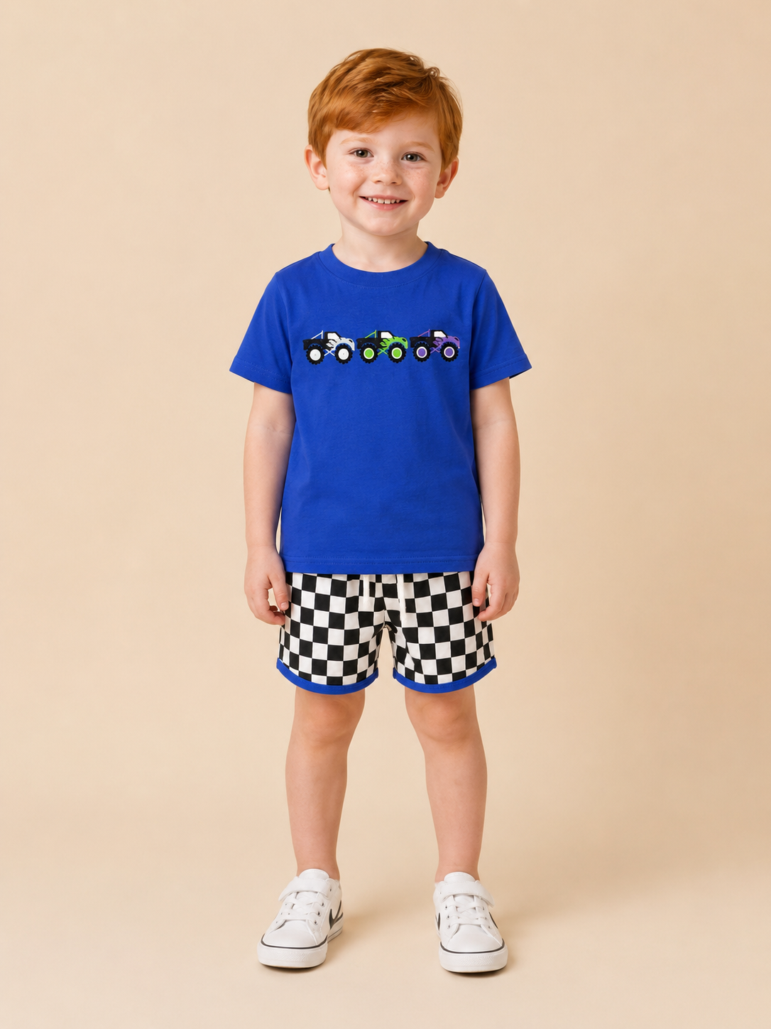 Boy wearing a blue shirt with monster trucks embroidered on the front and black and white checkered shorts.