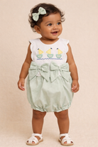 Baby girl wearing a light green outfit with a bow and sailboat design on a beige background