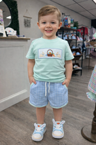 Child wearing a light blue shirt with an Easter graphic design and gingham shorts in a store setting.