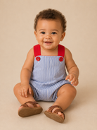 Infant baby boy wearing a seersucker patriotic bubble with brown sandals.