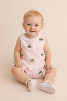 Baby wearing a pink outfit with green tractor patterns on a beige background