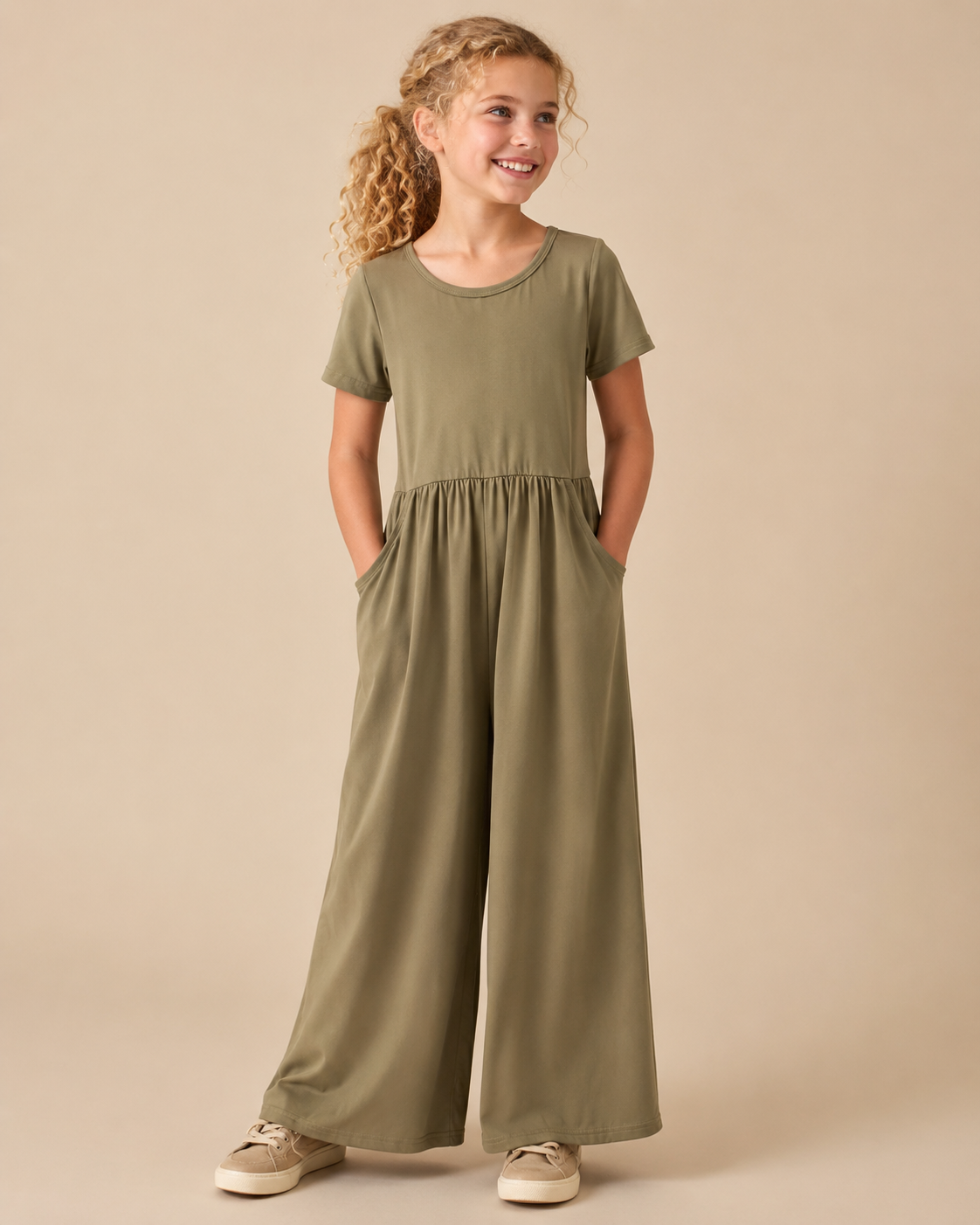 Tween girl wearing an olive green wide leg jumper on beige background.