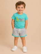 Child wearing a turquoise shirt with animal graphics and checkered shorts on a beige background