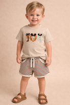 Child wearing a beige t-shirt with animal prints and striped shorts on a beige background