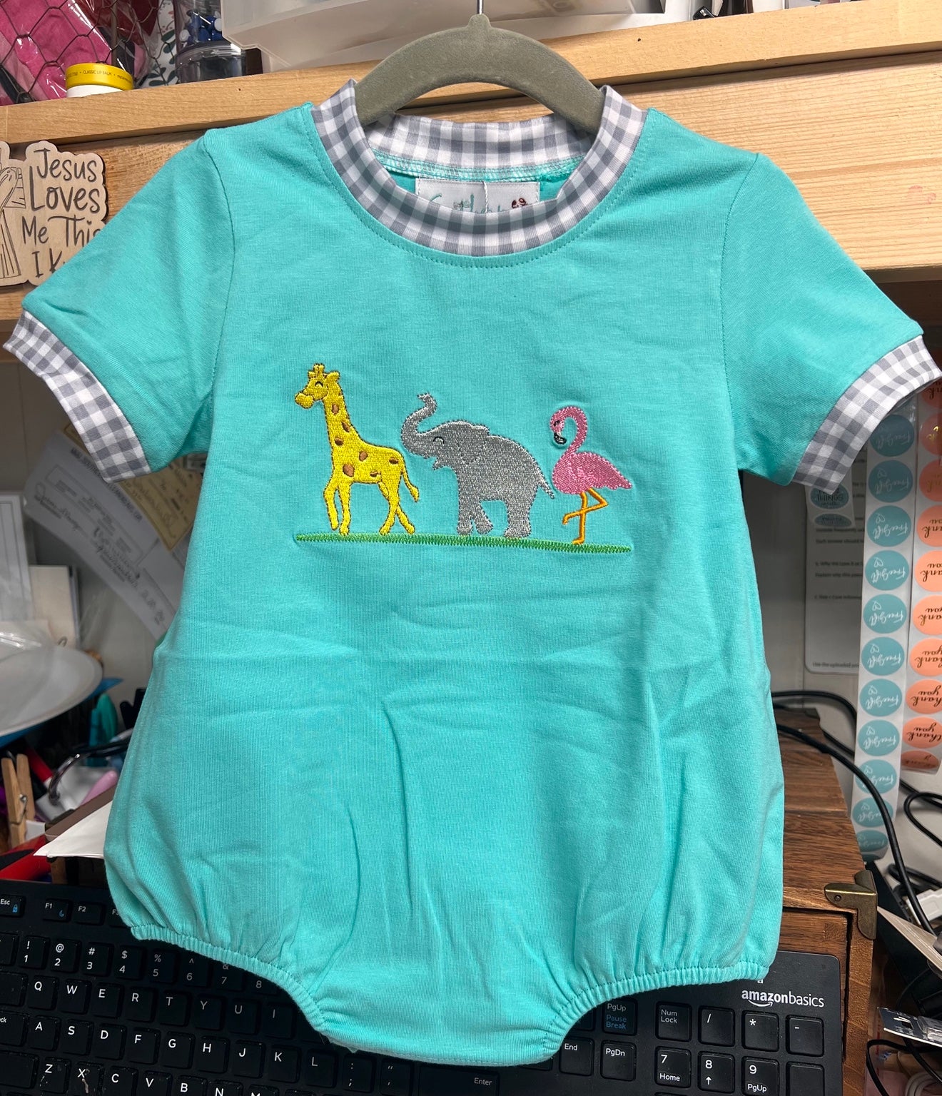 Teal baby romper with animal appliqués on a hanger.