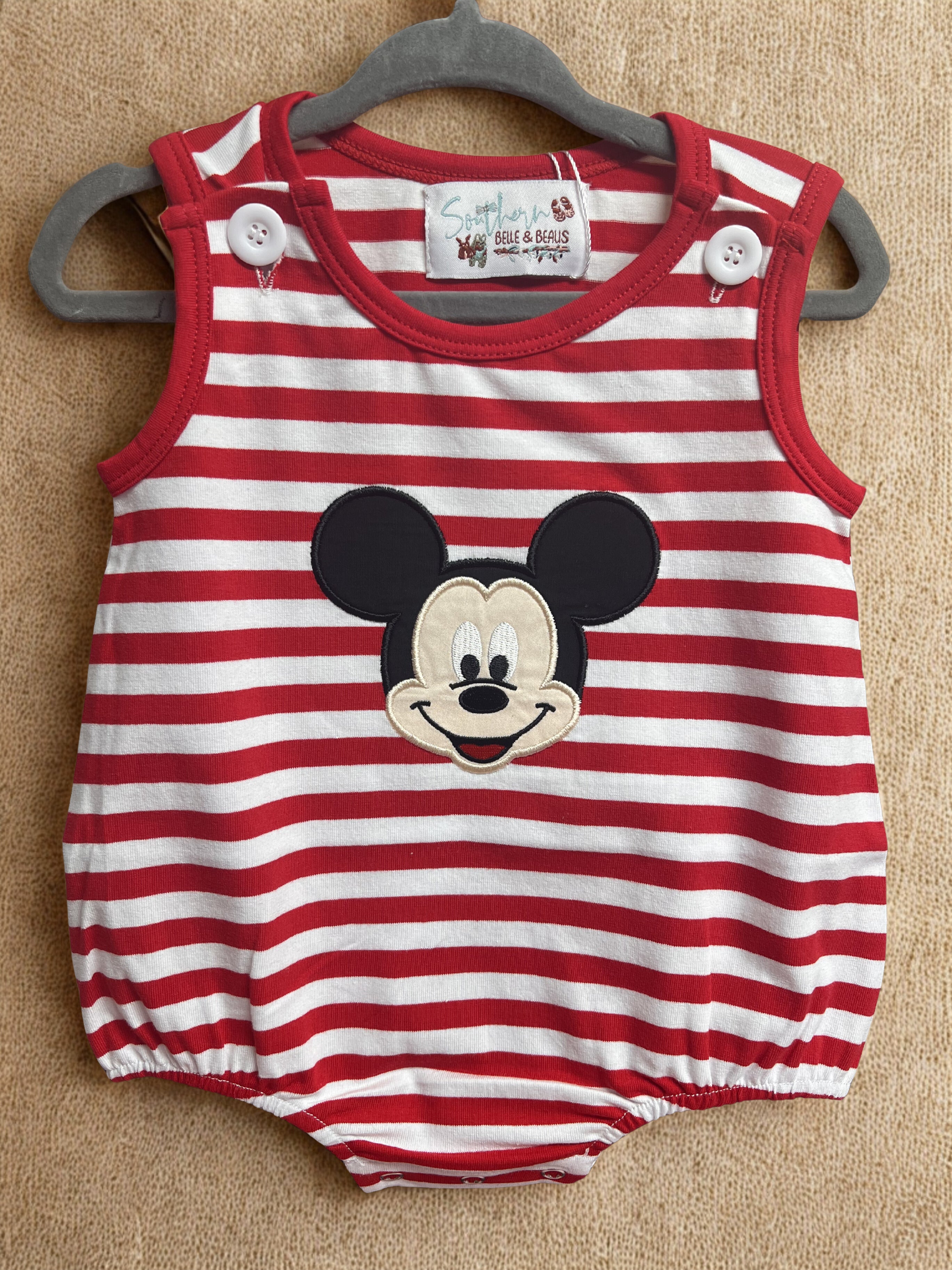 Red and white striped baby romper with a face on a beige background