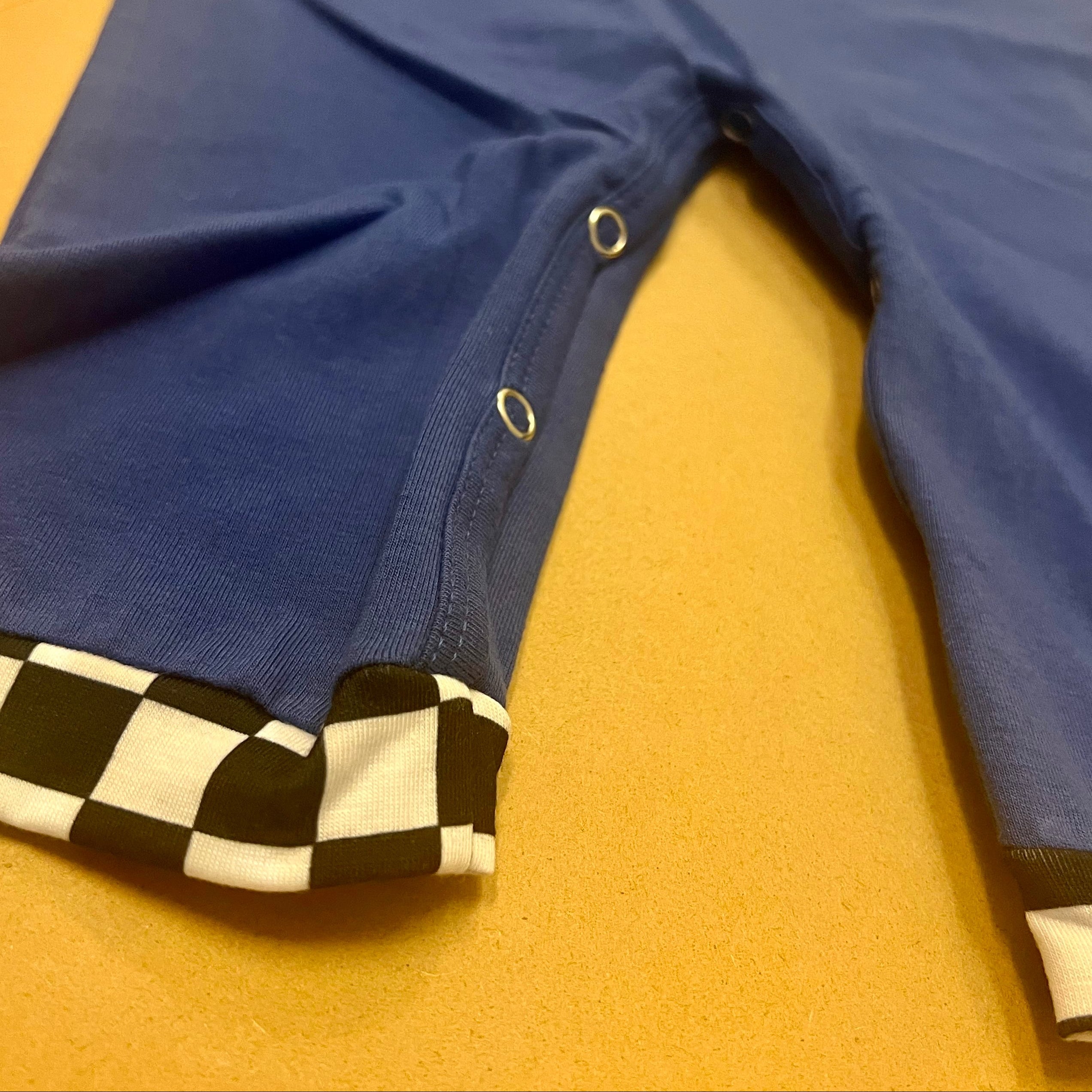 Royal blue baby boy romper with monster truck appliqués and black-and-white checkered trim.