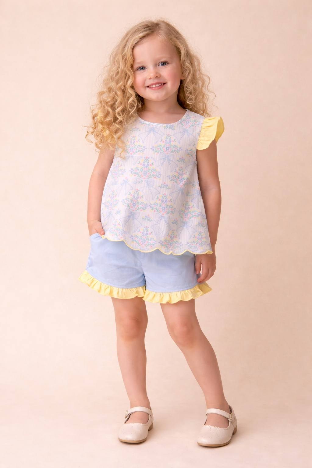 Young girl wearing a white top with yellow trim and light blue shorts on a beige background