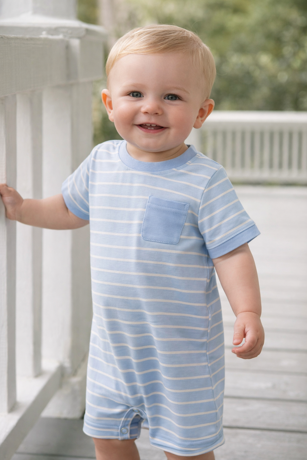 Child wearing a blue and white striped romper on a white railing.