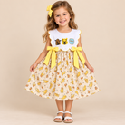 Girl wearing Sweet Honey Dress with a white scalloped bodice, honey-bear motifs, yellow waist bows, and a cream bear-print skirt.