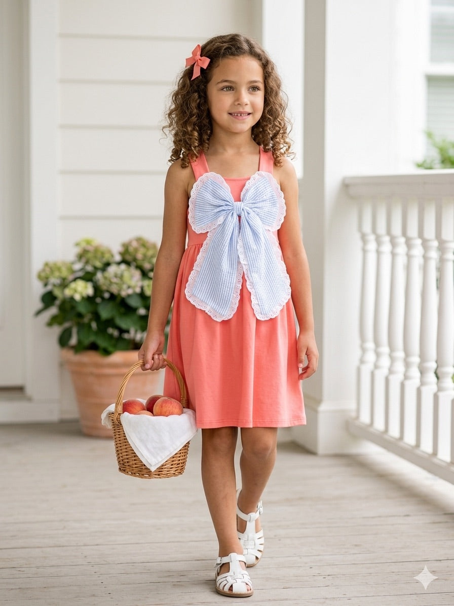 Young girl in a coral dress with a large white bow standing on a porch.