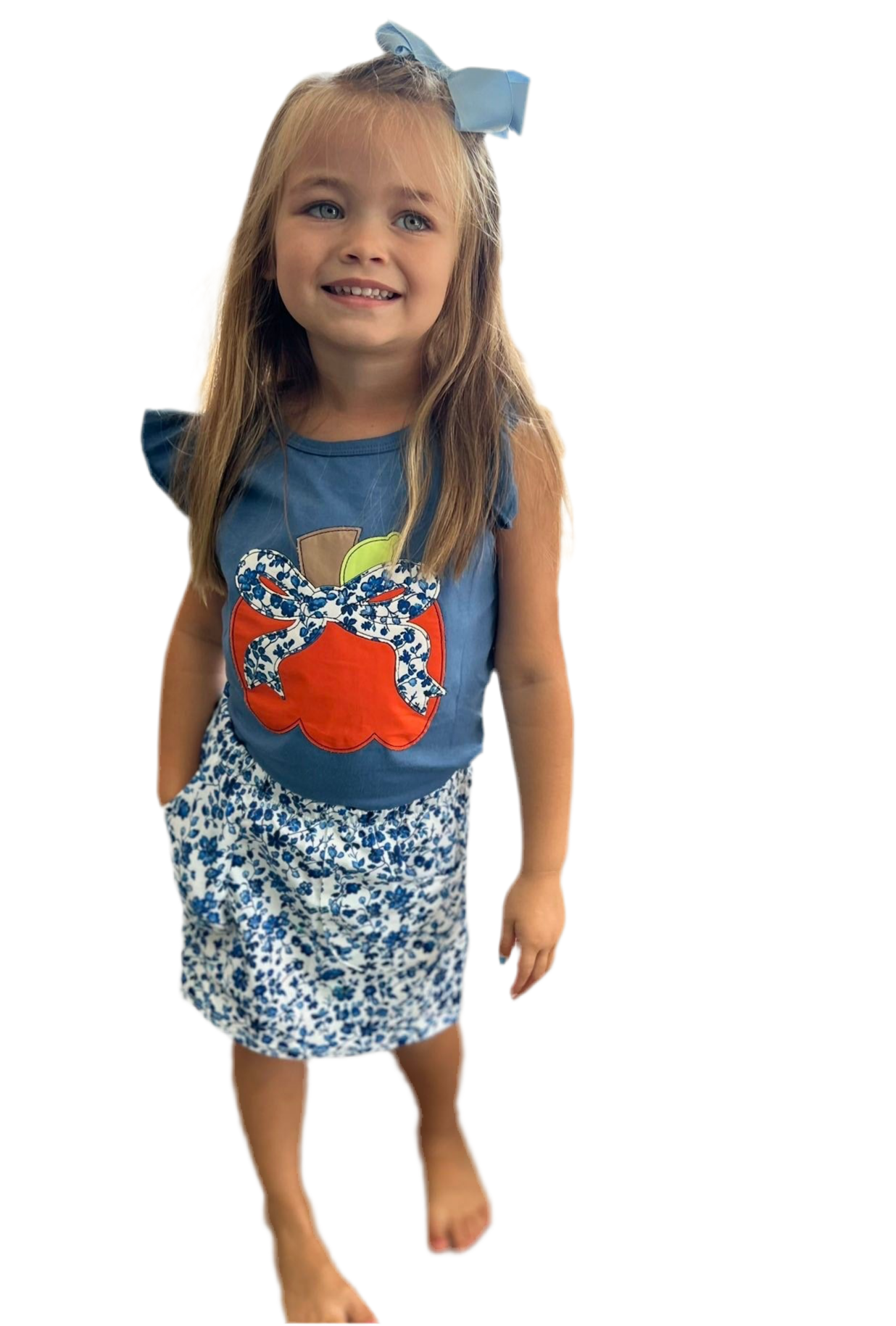 Young girl wearing a blue top with a orange pumpkin design and floral shorts on a white background