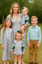 Family of five posing outdoors in matching outfits with green accents.