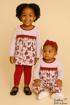 Two children wearing matching outfits with red and white patterns on a beige background.