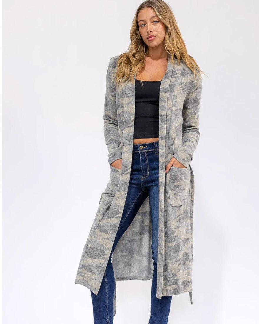 Woman wearing a long, light-colored cardigan over a black top and blue jeans on a white background