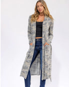 Woman wearing a long, light-colored cardigan over a black top and blue jeans on a white background