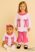 Two young girls wearing matching outfits with pink bows on a beige background