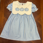 A toddler girl's blue and white gingham dress with a white bib collar featuring three embroidered blue pumpkins, laid flat on a wooden table.
