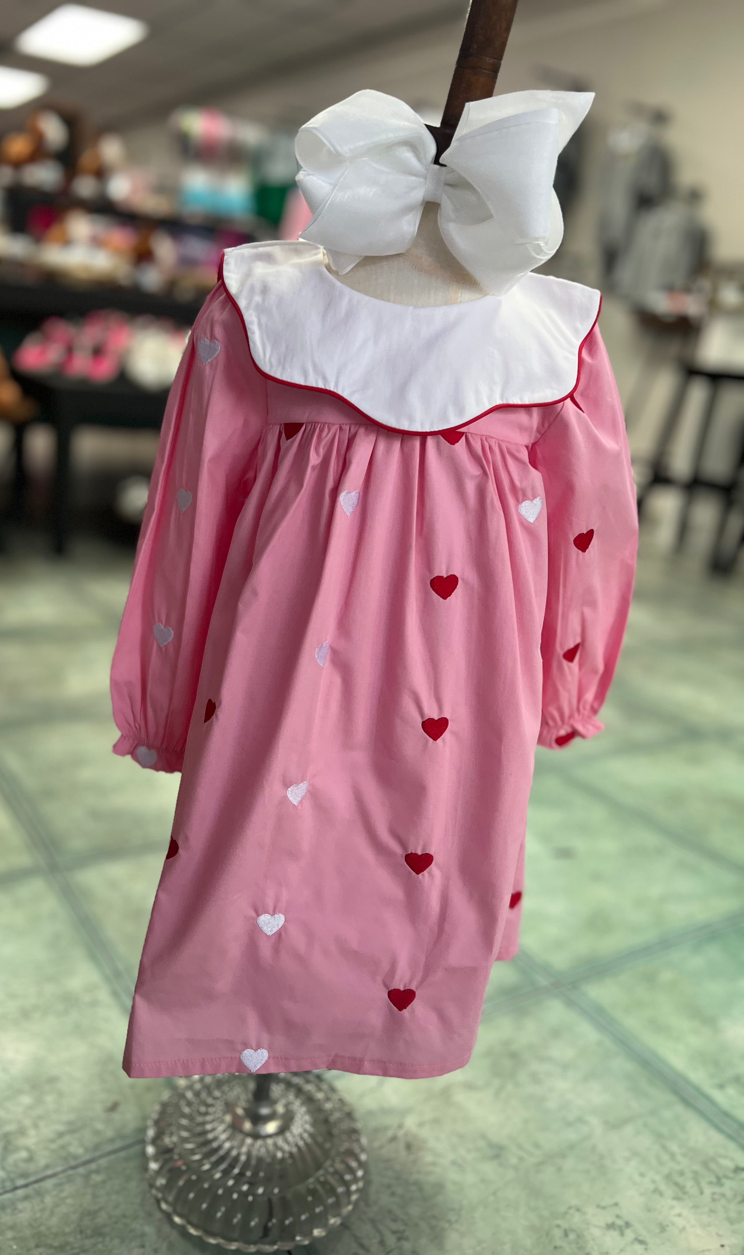 Pink dress with white collar and heart patterns on a mannequin in a store setting.