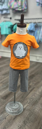 Children's outfit with orange shirt and striped pants on a mannequin against a store background.