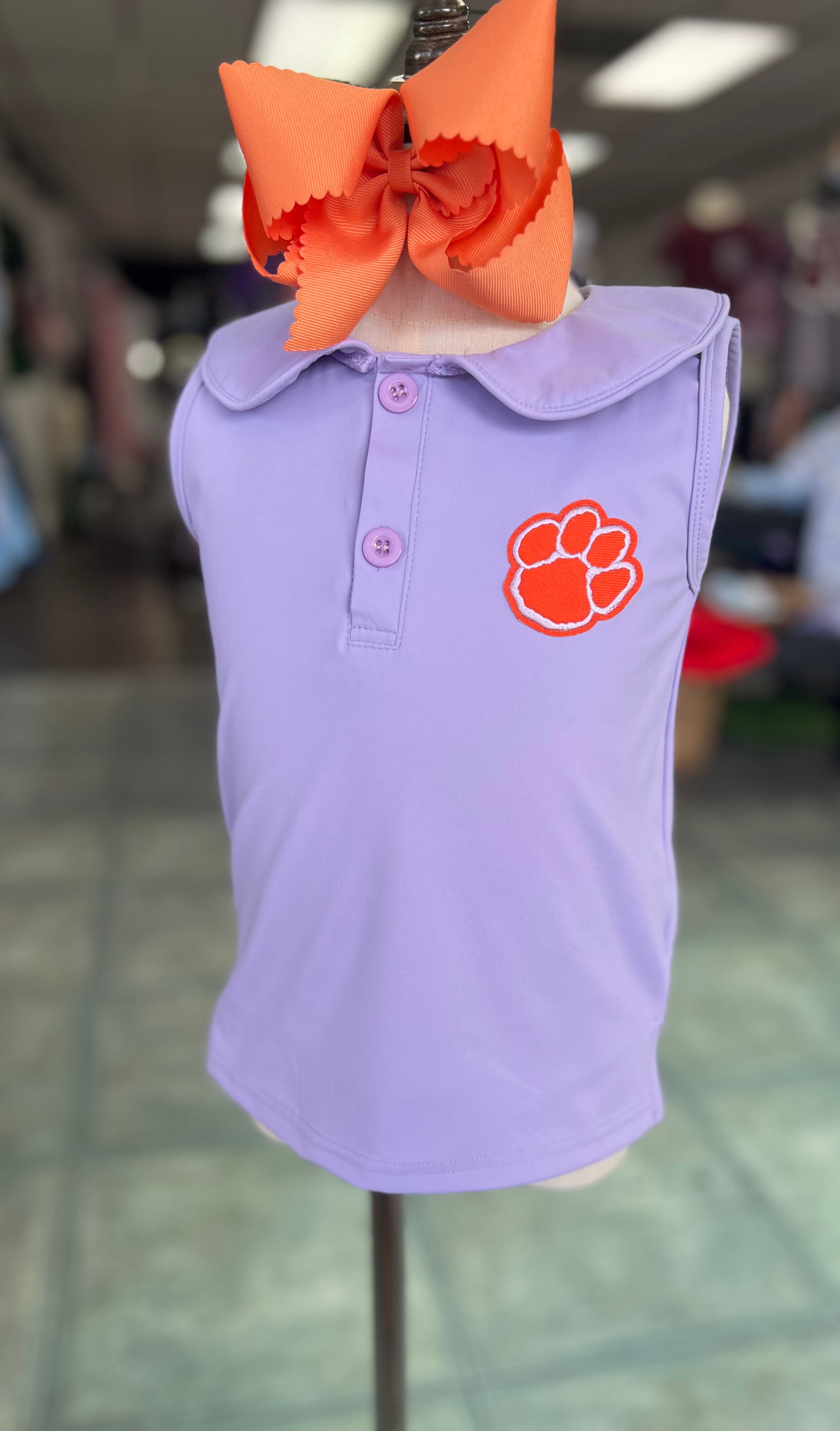 Purple polo shirt with orange logo on a mannequin head with an orange bow.