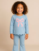 Child wearing a light blue outfit with a pink bow on a beige background