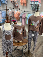 Children's clothing set with brown sweatshirt and patterned pants on mannequins in a store setting.
