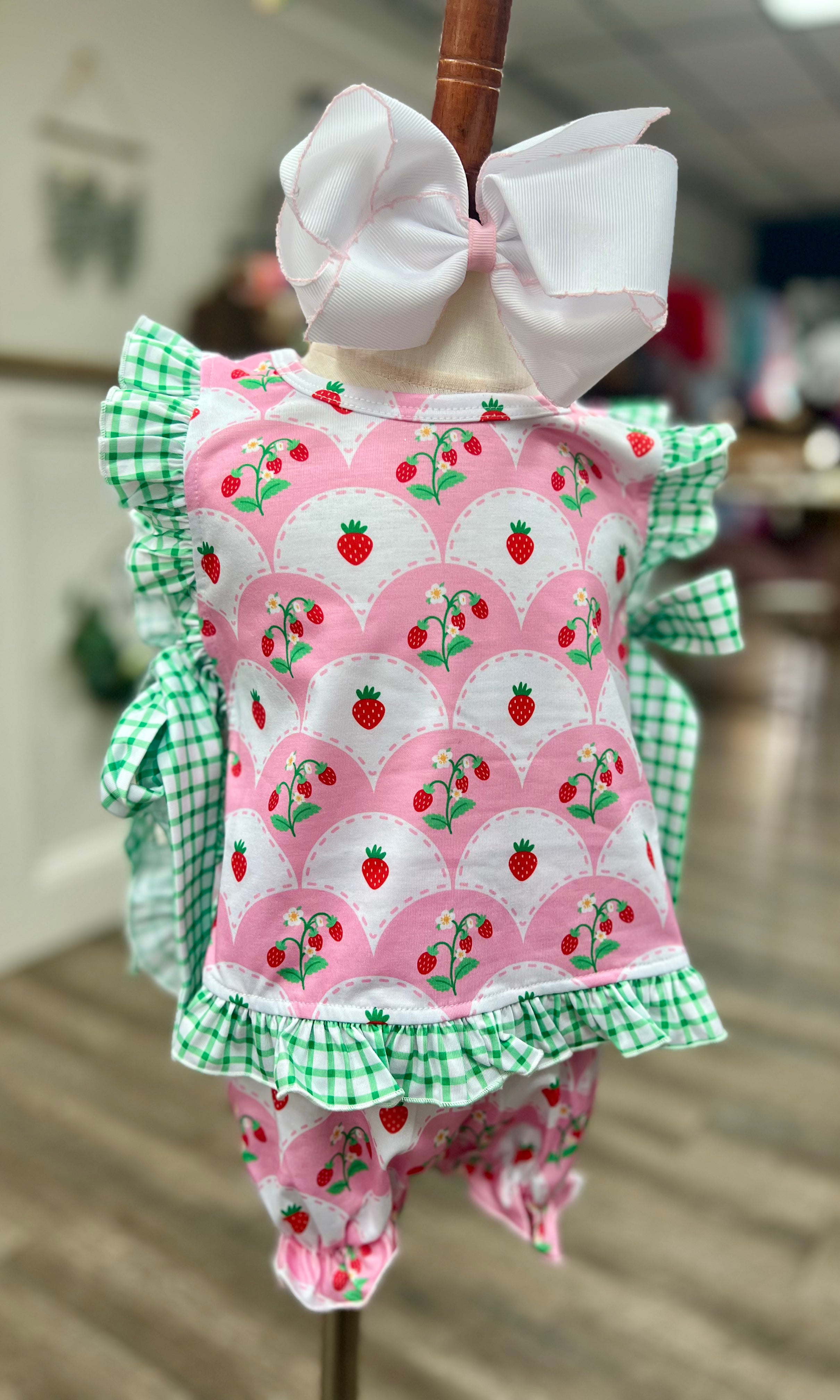 Children's outfit with pink strawberry pattern and green checkered details on a mannequin.