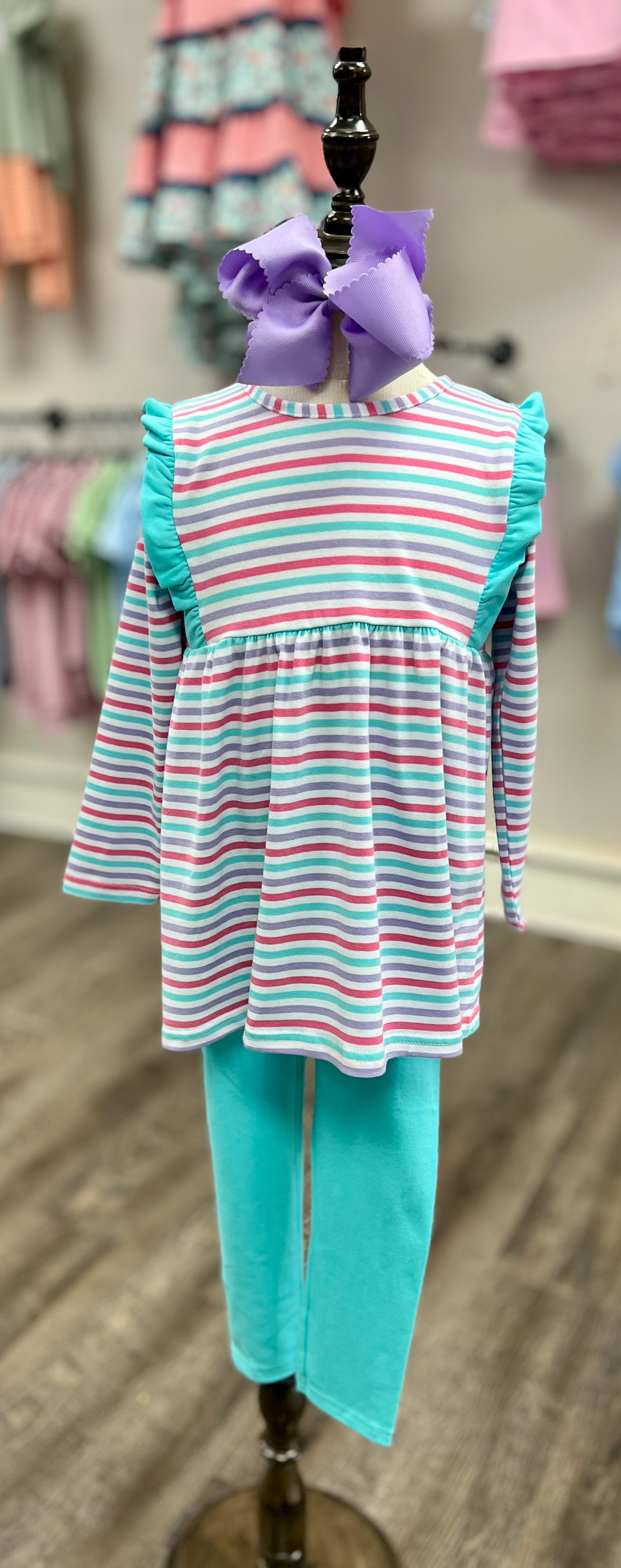 Striped dress and leggings set on a mannequin with a bow, against a store background.