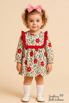 Child wearing a festive dress with red and green floral pattern on a beige background